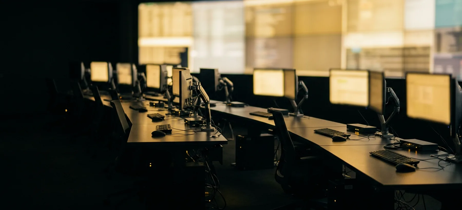 A security operations floor facing a lit monitor wall